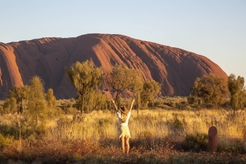 women standing near uluru with hands in the air